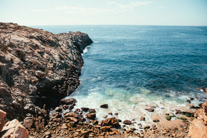 A view of the ocean with rocks surrounding it. Farmhouse style wood signs made on the California Central Coast.