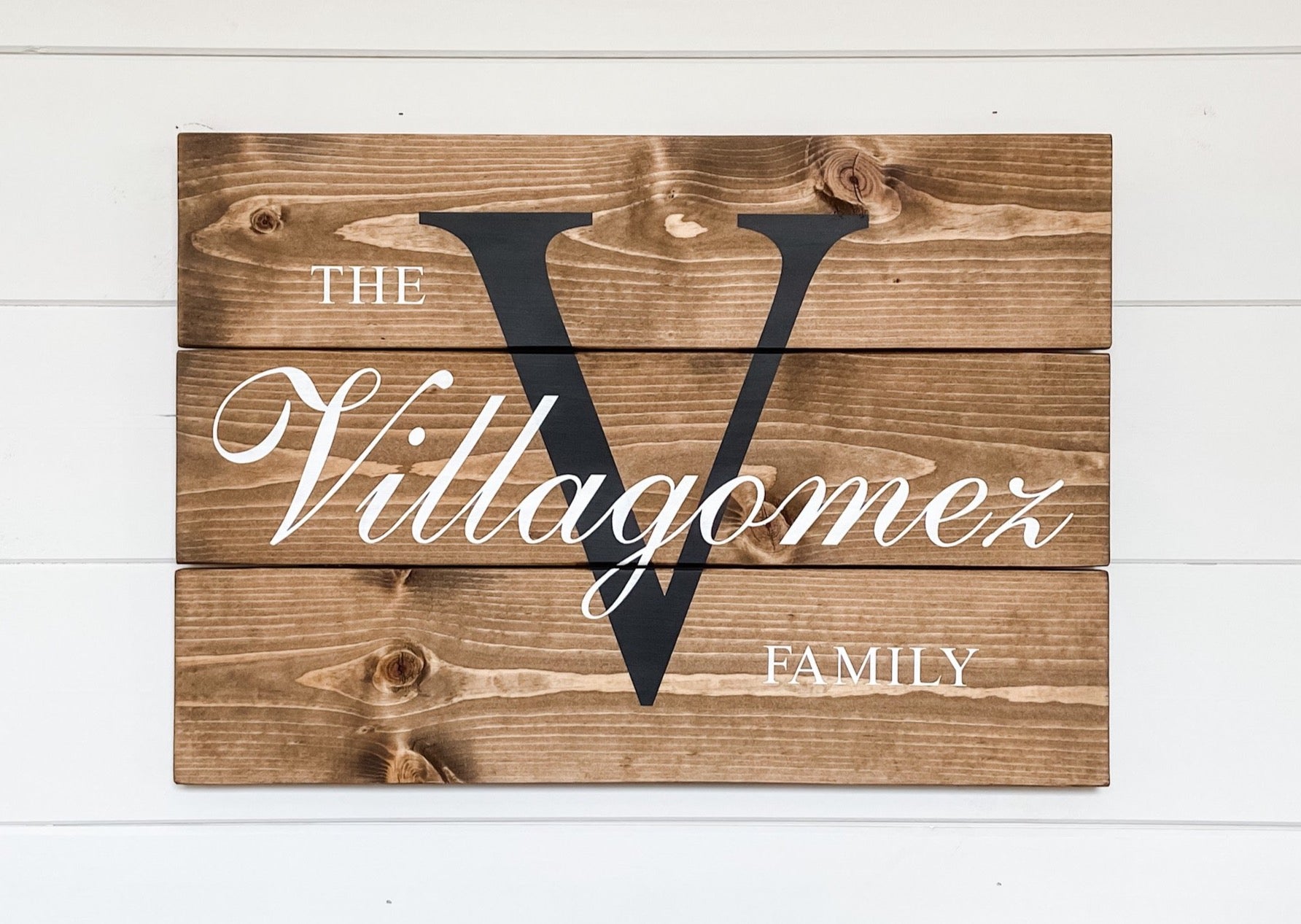 Farmhouse style sign made out of wood planks. Family name and initial painted onto the sign